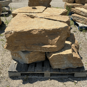 Large natural sandstone boulders stacked on a wooden pallet at a nursery.