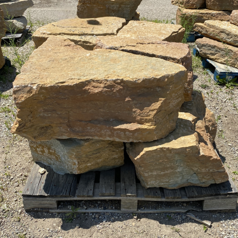 Large natural sandstone boulders stacked on a wooden pallet at a nursery.